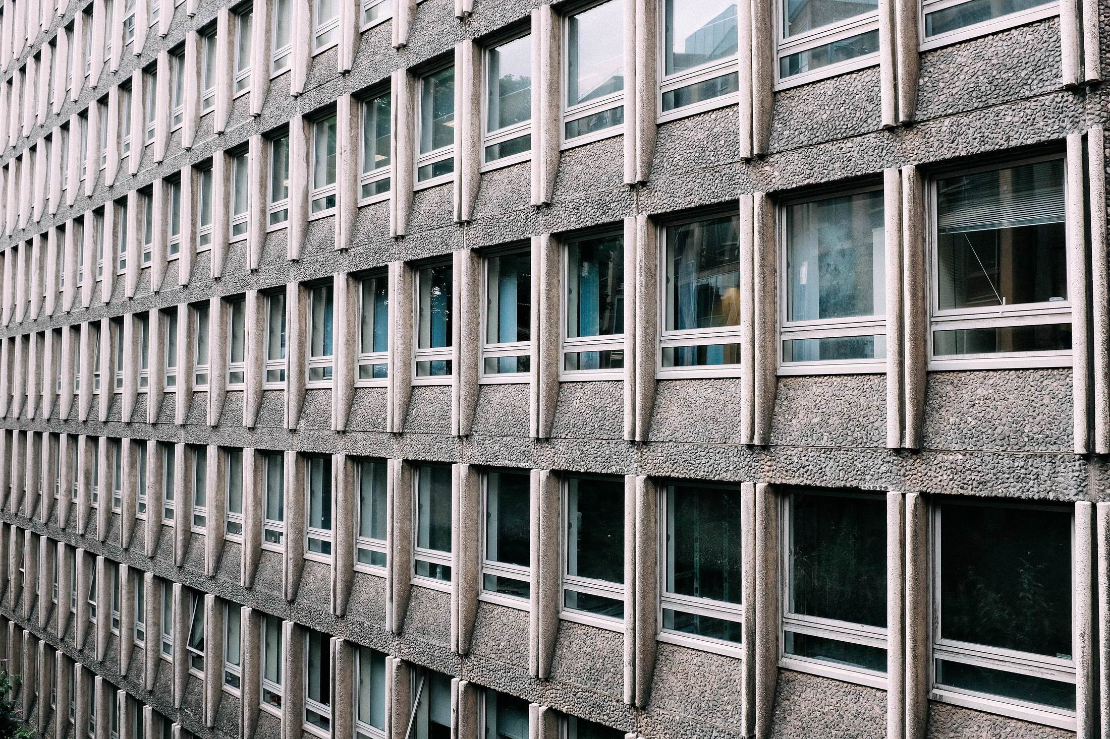 Close study of a mid-century stone office facade: a regular grid of recessed windows in aggregate concrete.