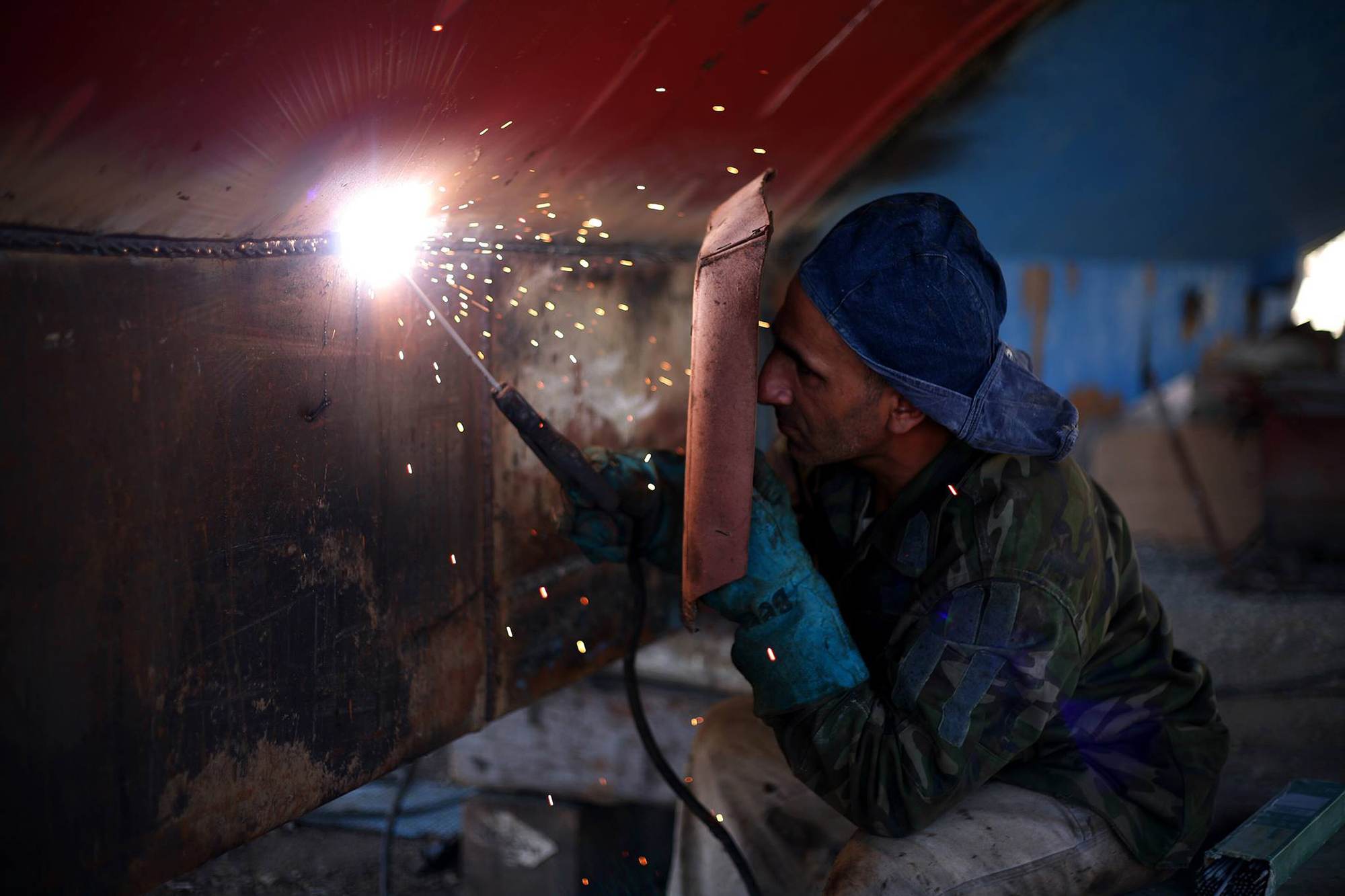 A welder working inside a steel structure, sparks falling past the frame.