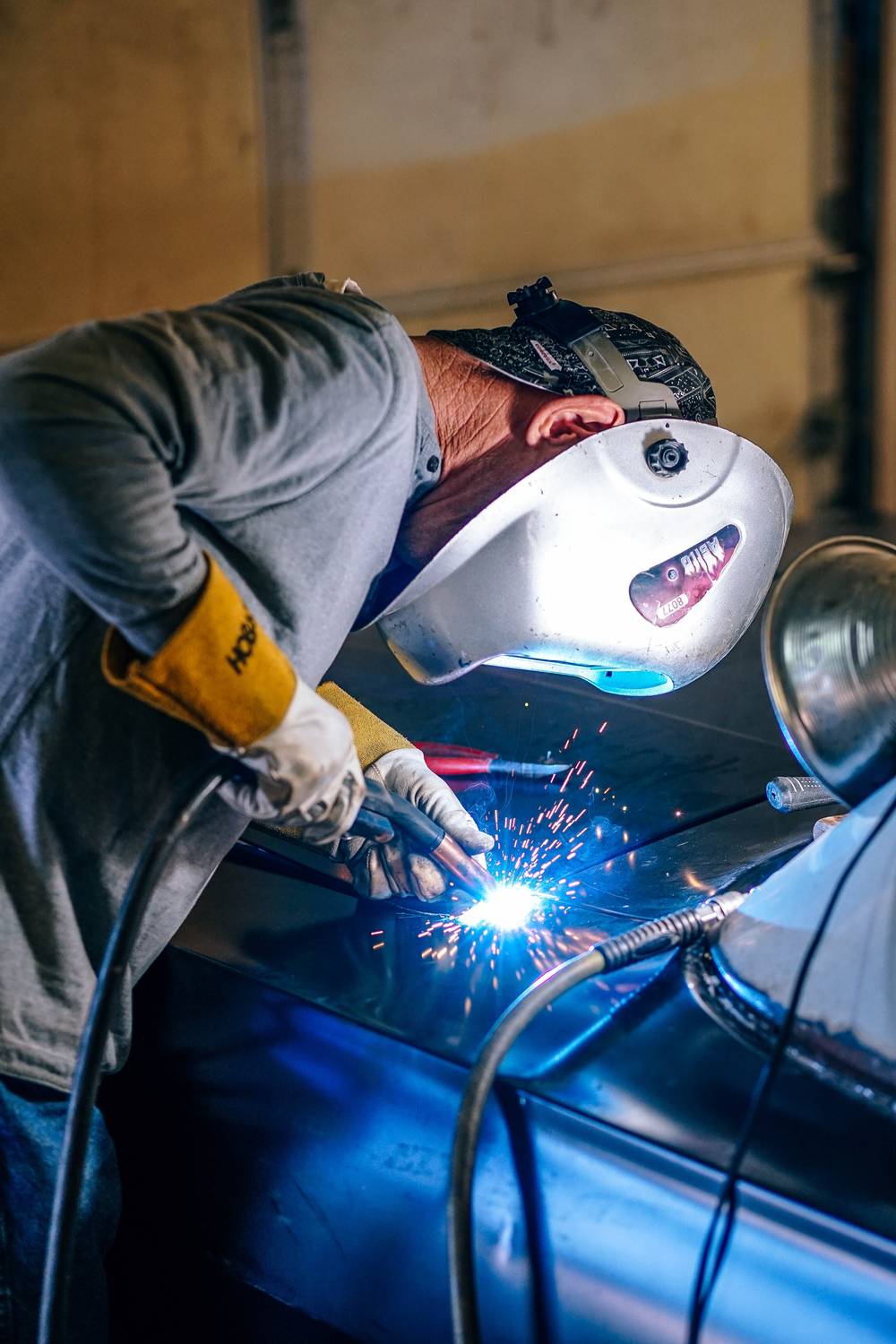 A welder in a hood laying a bead, arc light throwing hard shadows across the bay.