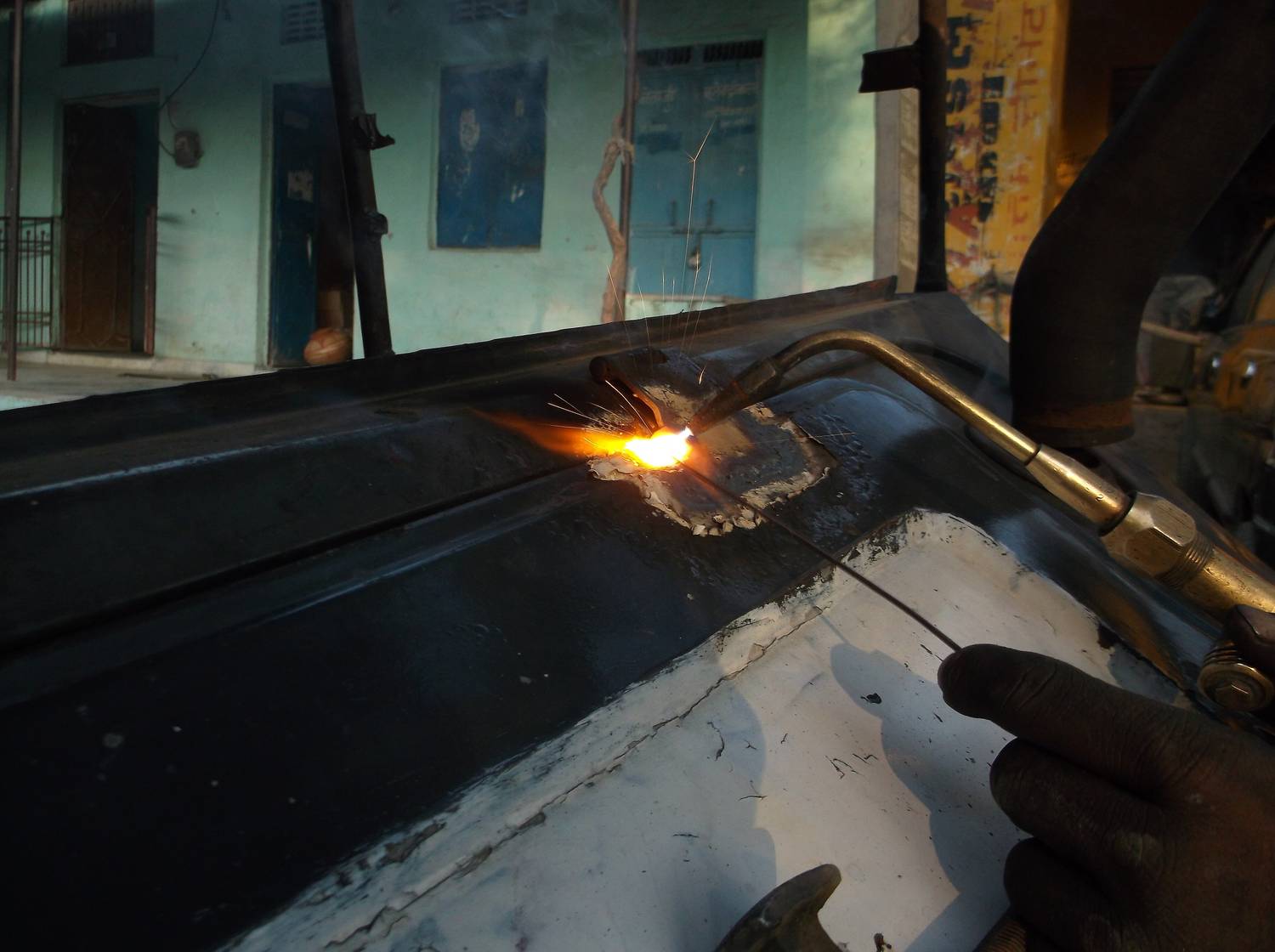 Gloved hands guiding a cutting torch along a marked steel panel.