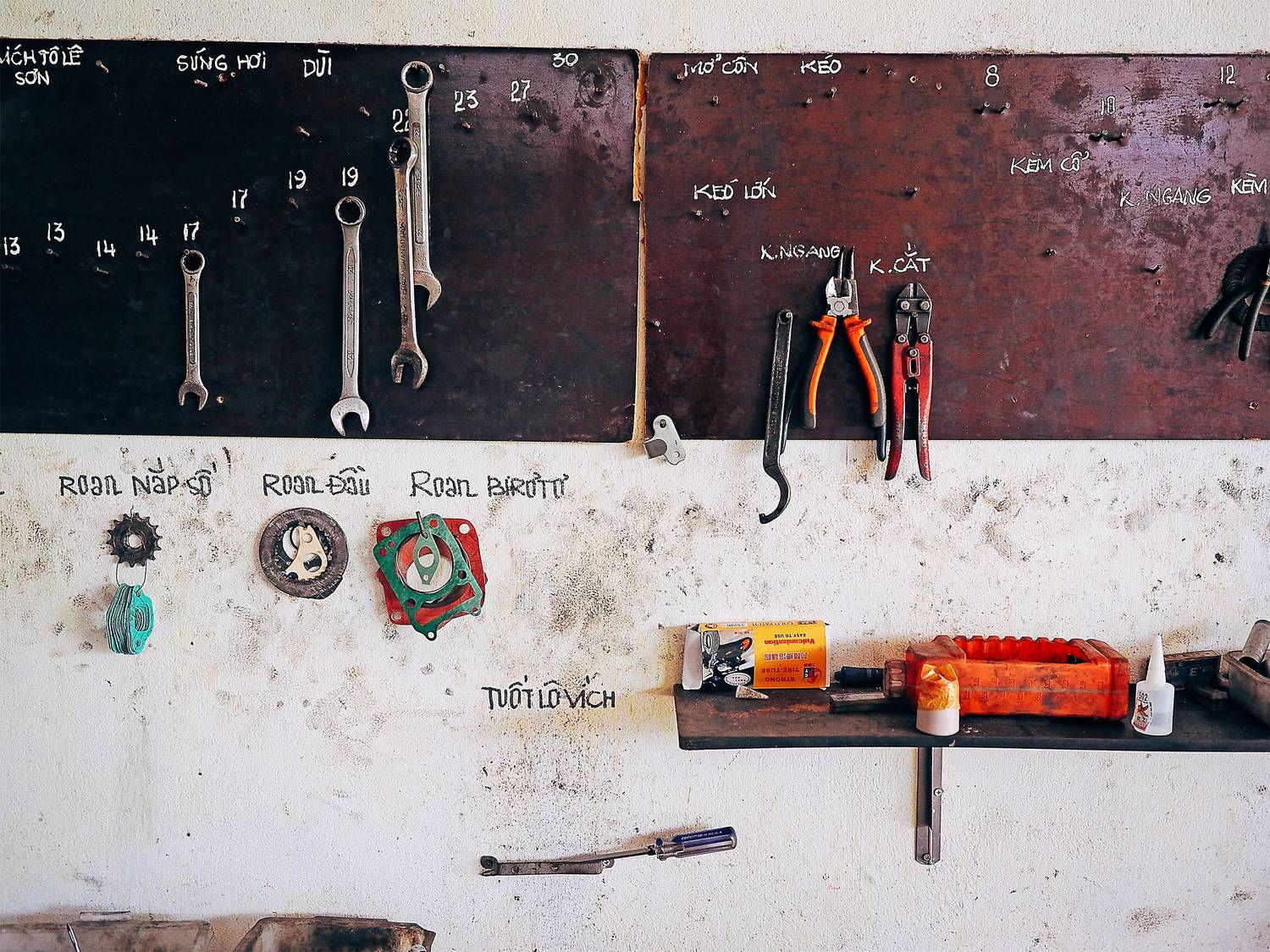 A painted tool board with wrenches and pliers hung on outlines, writing chalked beside them.