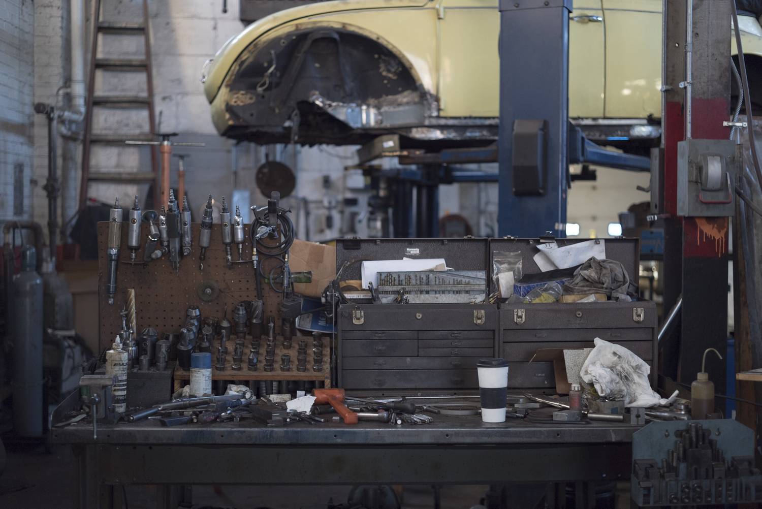 A cluttered mechanic's workbench with hand tools, parts trays and a vice.