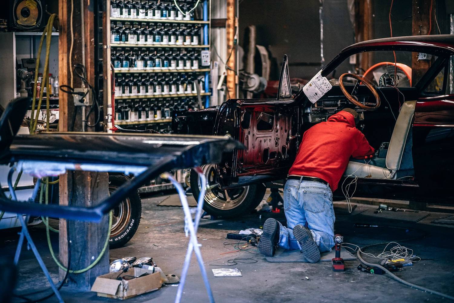 A vehicle stripped to bare metal on stands in a workshop, one person working beneath it.