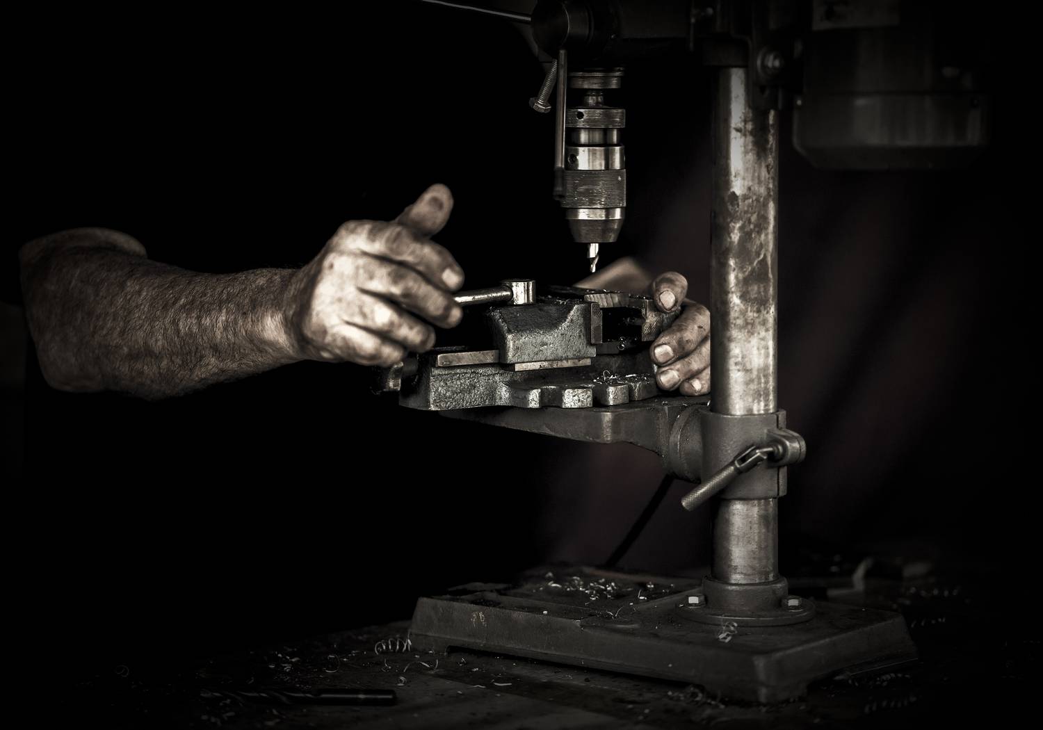 A hand striking a hammer against metal, the rest of the shop lost in darkness.
