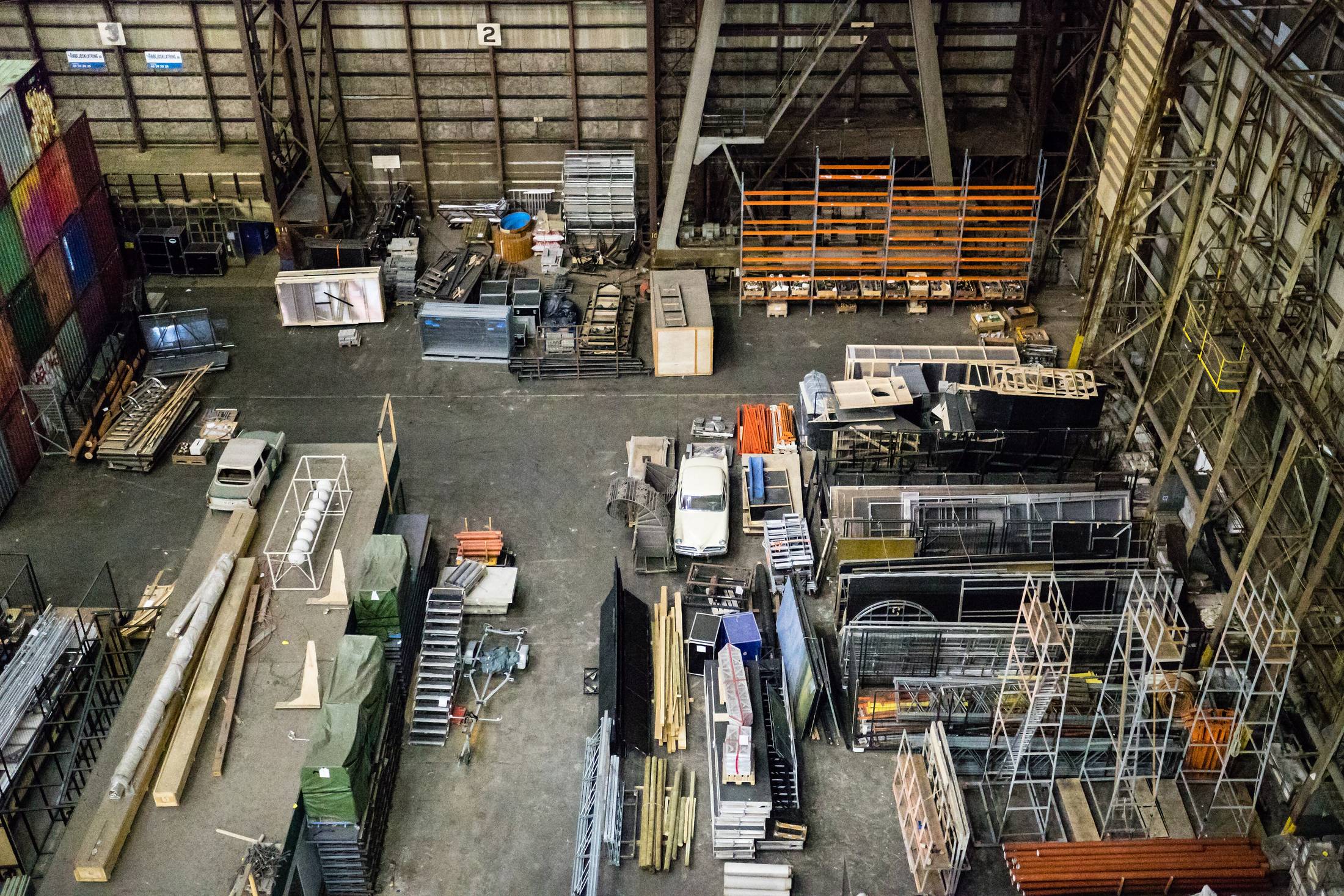 Interior of a working equipment yard: racking, stock steel and service vehicles under a steel roof.