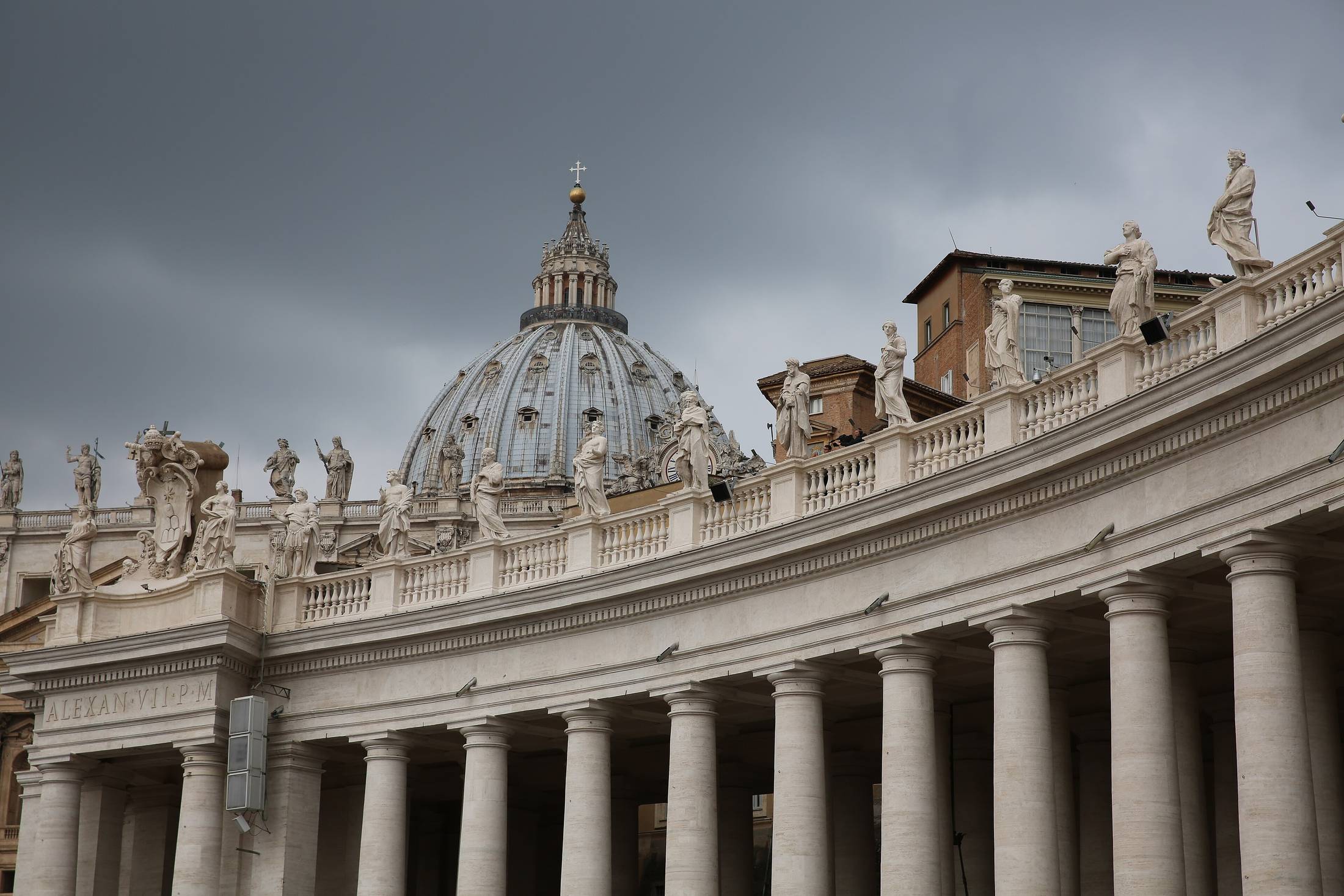 A curved stone colonnade in raking light, columns receding in repeated ranks beneath a heavy sky.