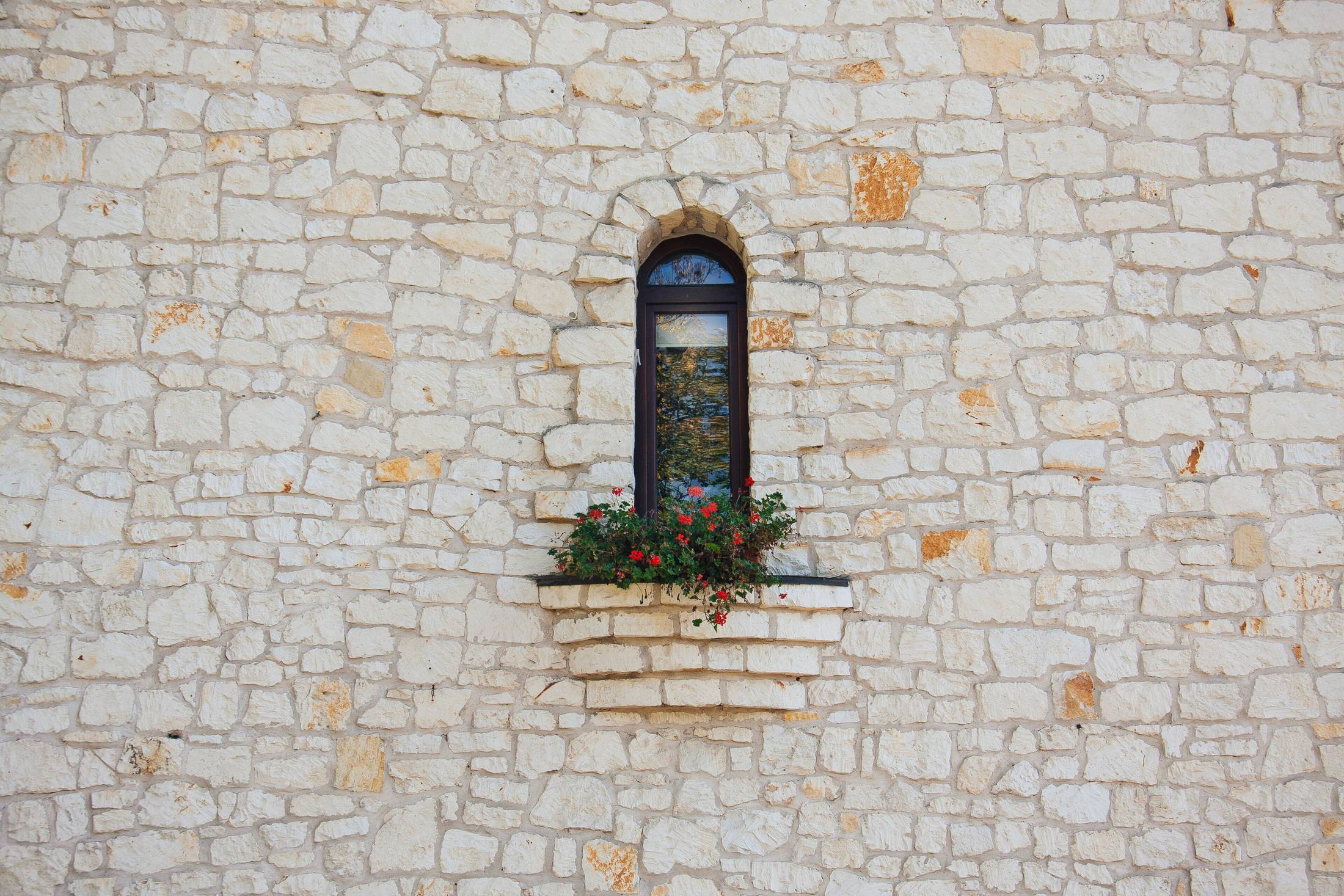 A dressed limestone wall with a single arched window, the coursing irregular and hand-cut.